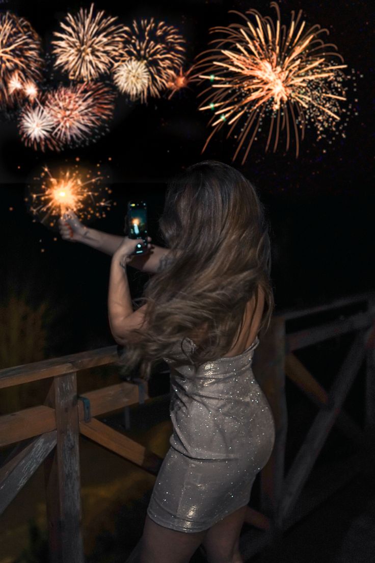 a woman taking a photo with her cell phone while fireworks go off in the background