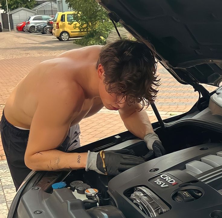 a man working on an engine in the hood of a car with his hands under the hood