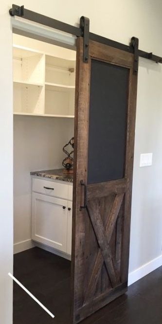 an open sliding barn door with chalkboard on the side and white cabinets behind it