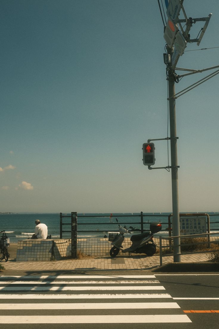 a person sitting on a bench next to the ocean near a traffic light and street sign