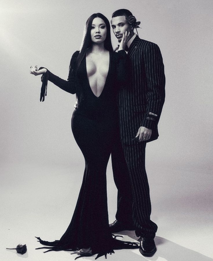 a man and woman dressed in black posing for a fashion photo with a bird on her arm