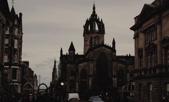 an old church in the middle of a city with people walking around it and cars driving down the street