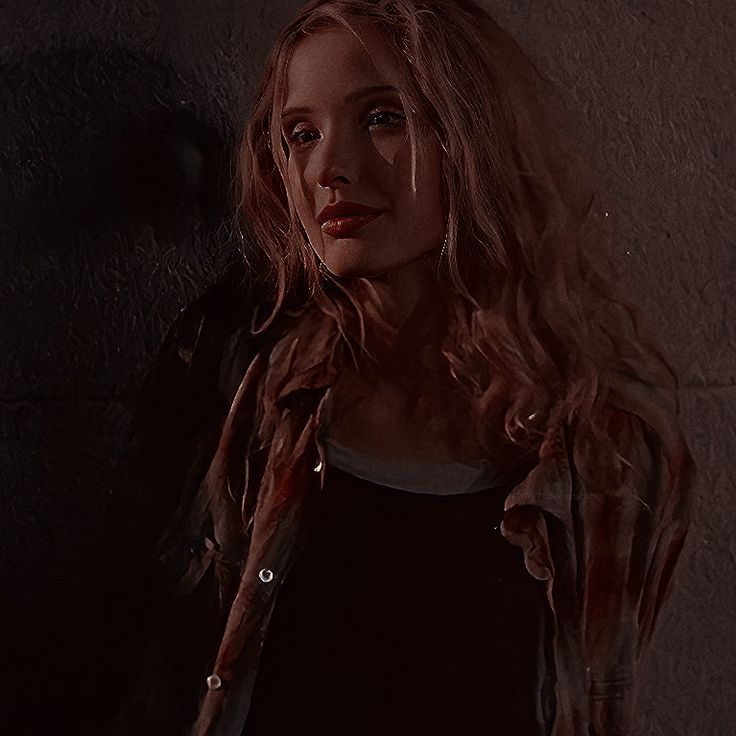 a woman standing next to a wall with her hair blowing in the wind and looking at the camera