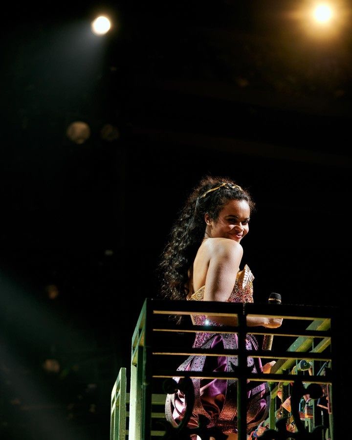 a woman standing on top of a stage in front of a green box with lights