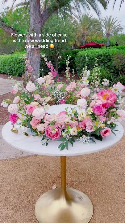 a white table topped with lots of pink and white flowers on top of a metal stand