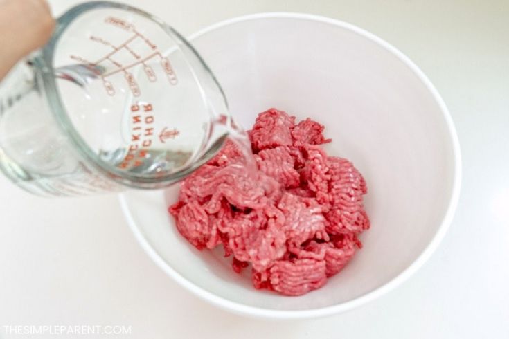 a person is pouring water into a bowl filled with ground beef and it's contents