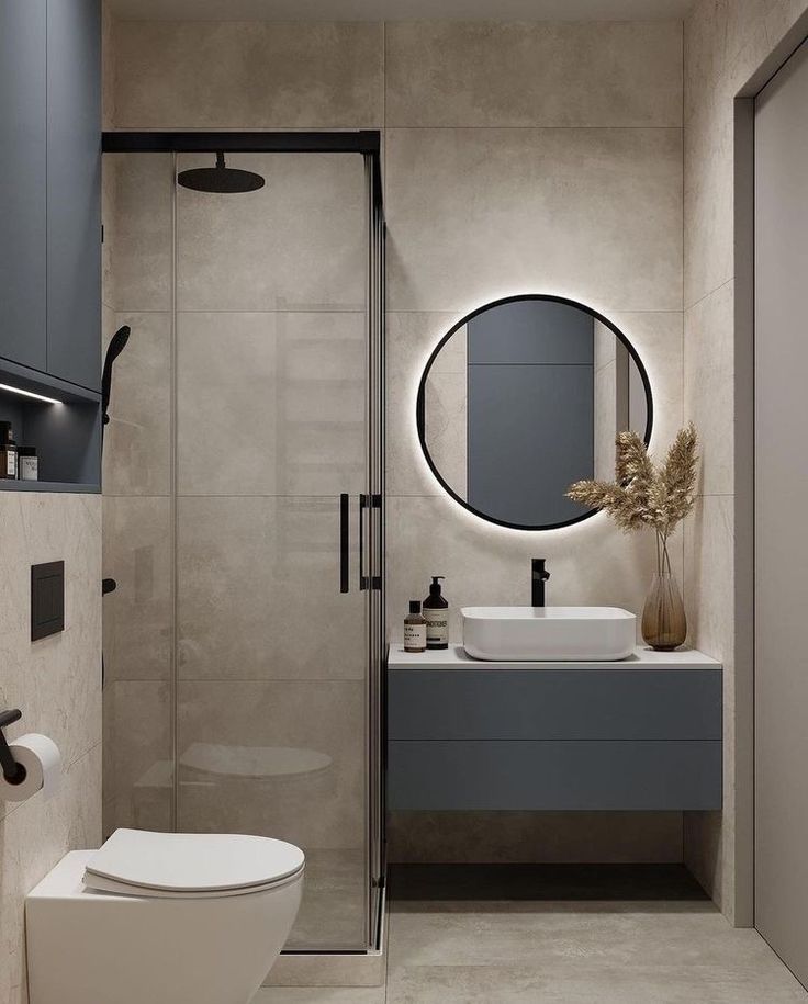 a white toilet sitting next to a walk in shower under a round mirror above a sink