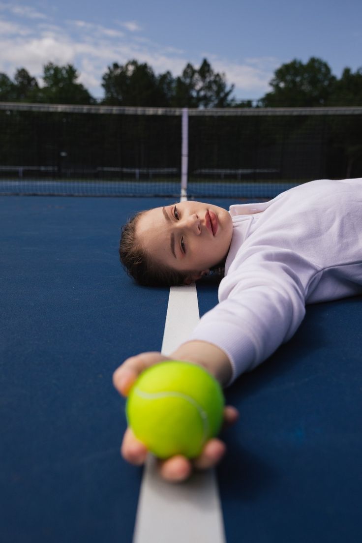 a young boy laying on top of a tennis court holding a green ball