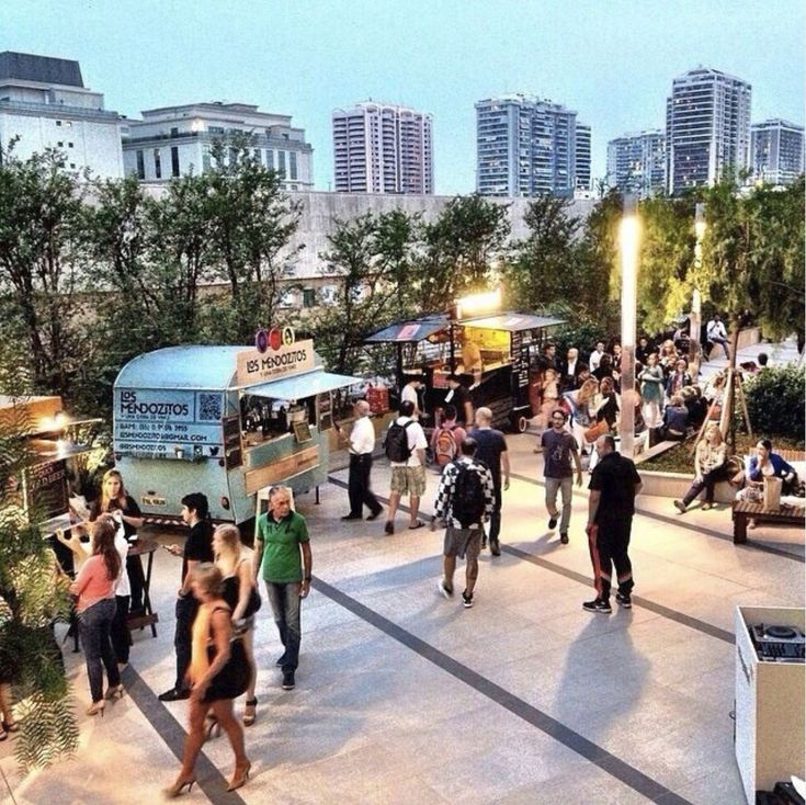 many people are walking around in the city at night with their food trucks parked nearby