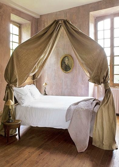 a canopy bed in a bedroom with wooden floors and walls, along with two windows