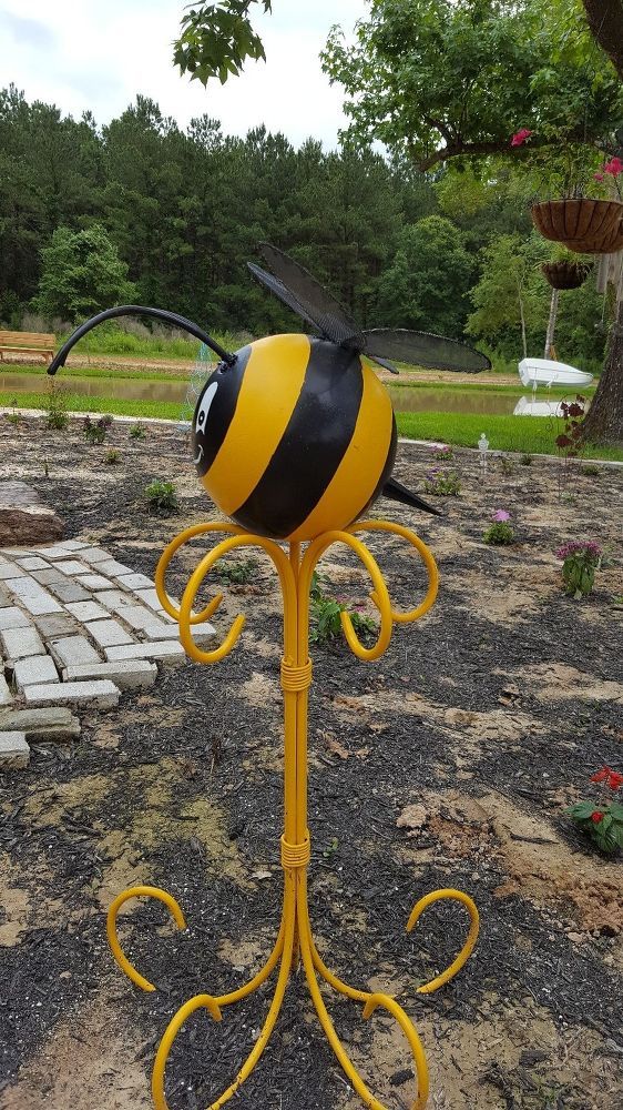 a yellow and black bee statue sitting on top of a gravel field