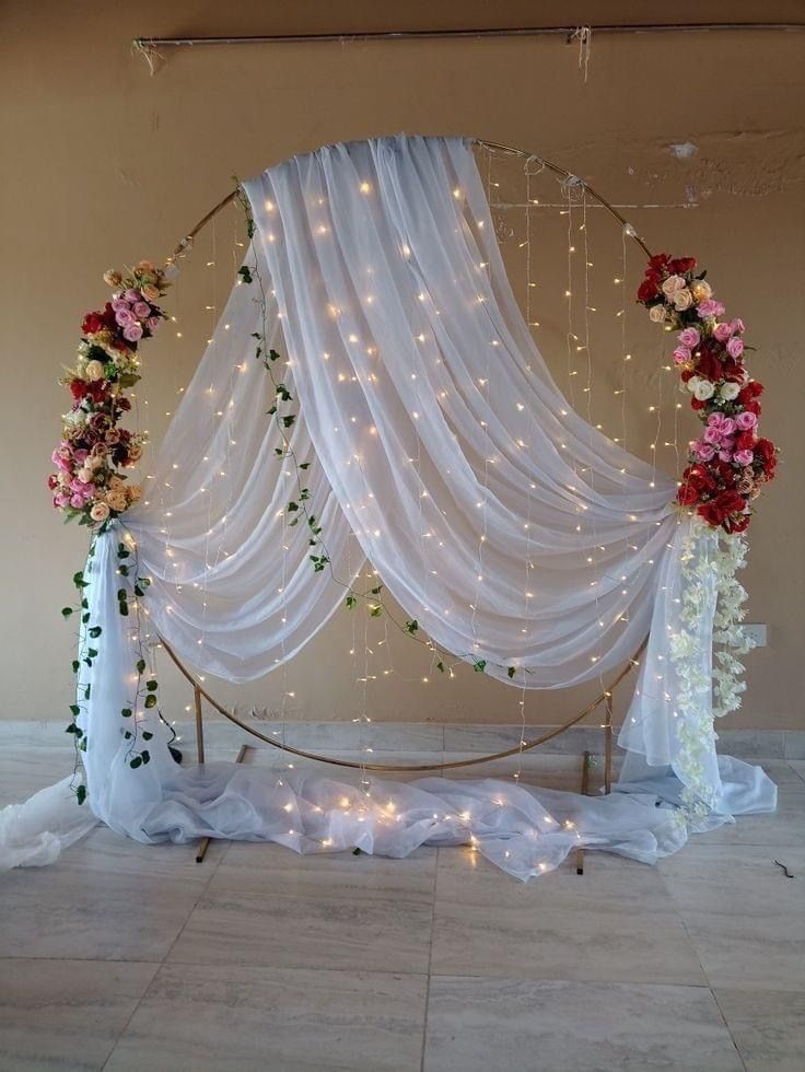 a white drape with flowers and lights hanging from it's sides on the floor