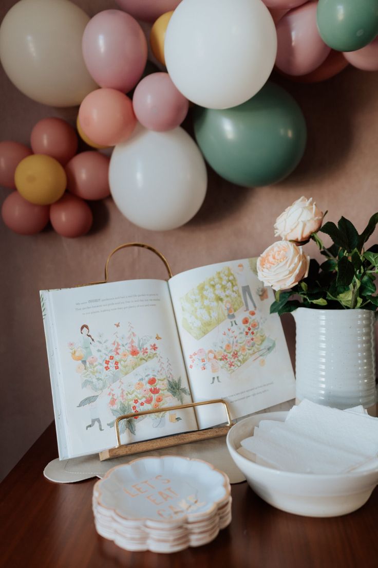 an open book sitting on top of a wooden table next to plates and vases