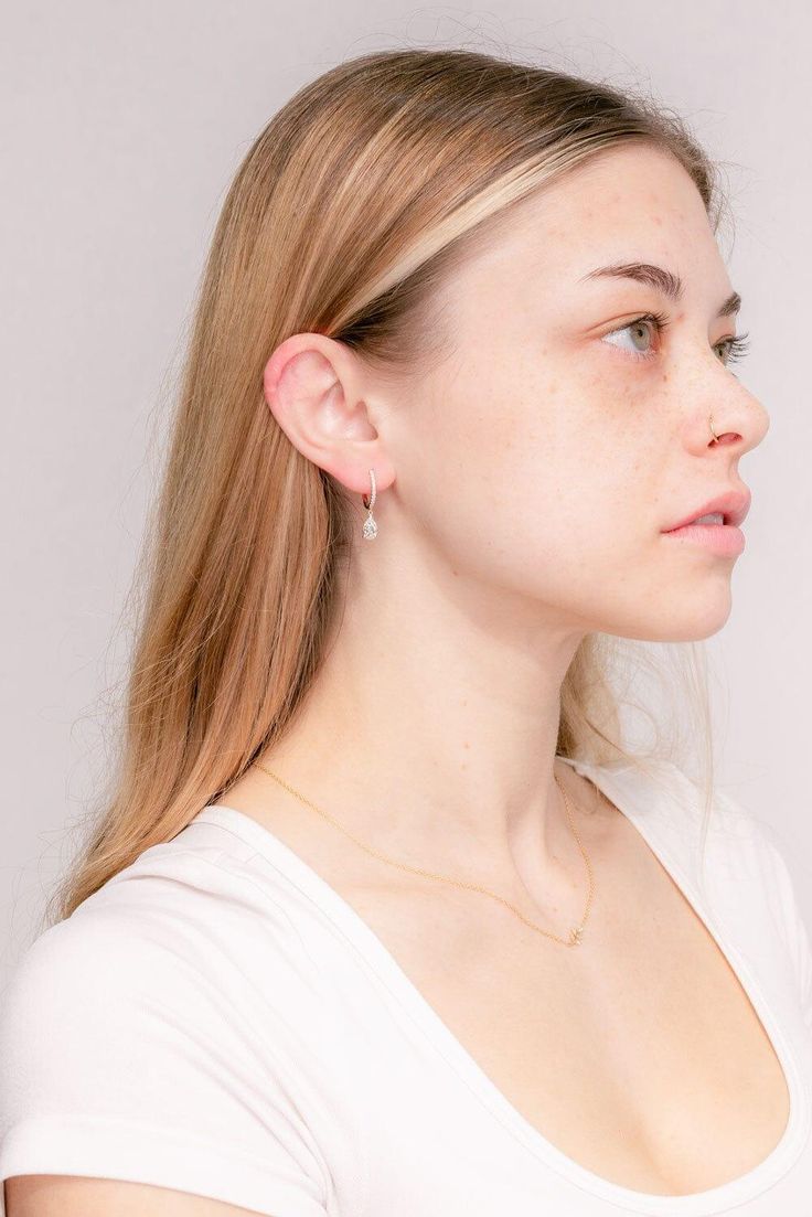 a young woman with blonde hair wearing a white shirt and diamond earrings, looking off to the side