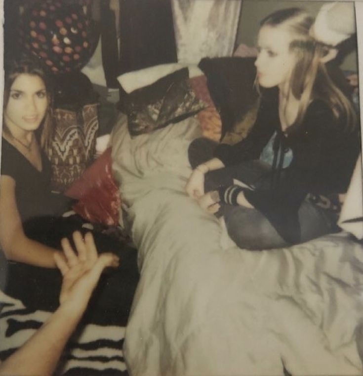 two young women sitting on a bed next to each other and one is reaching for something