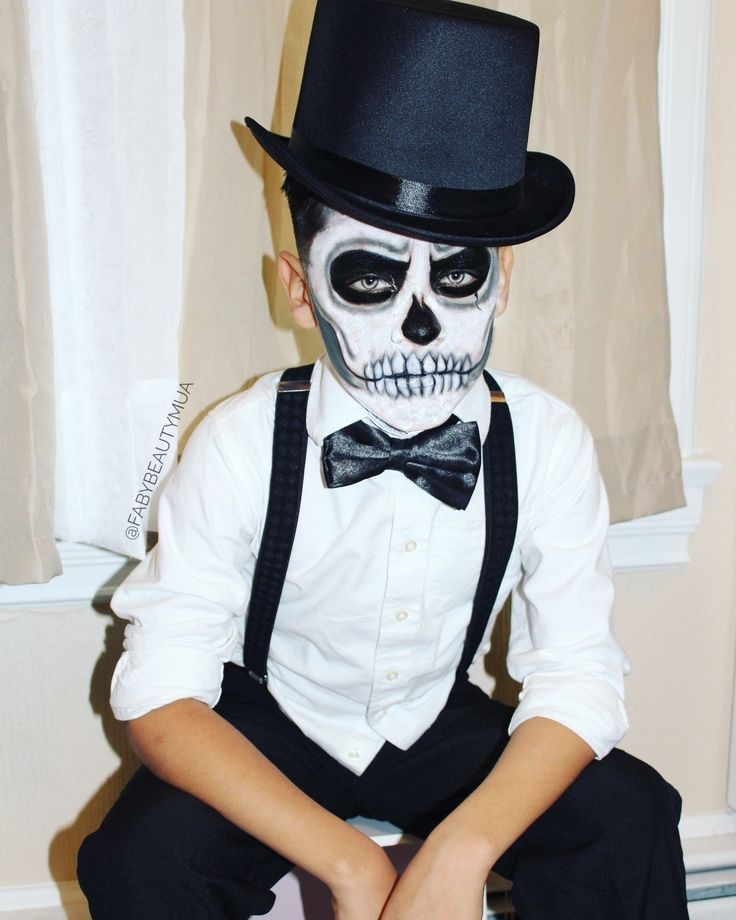 a young boy dressed up as a skeleton with a top hat and bow tie sitting on the floor