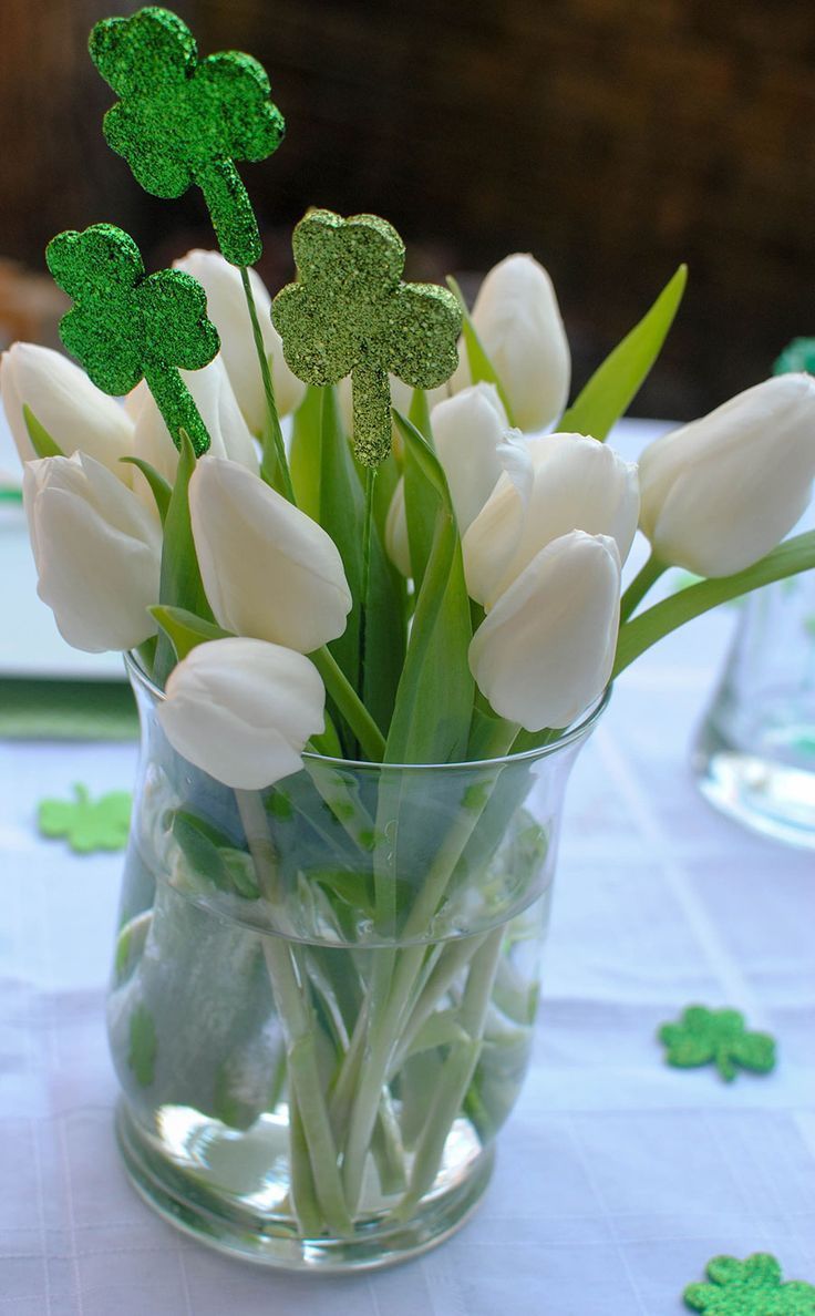 a vase filled with white tulips and green shamrocks on top of a table