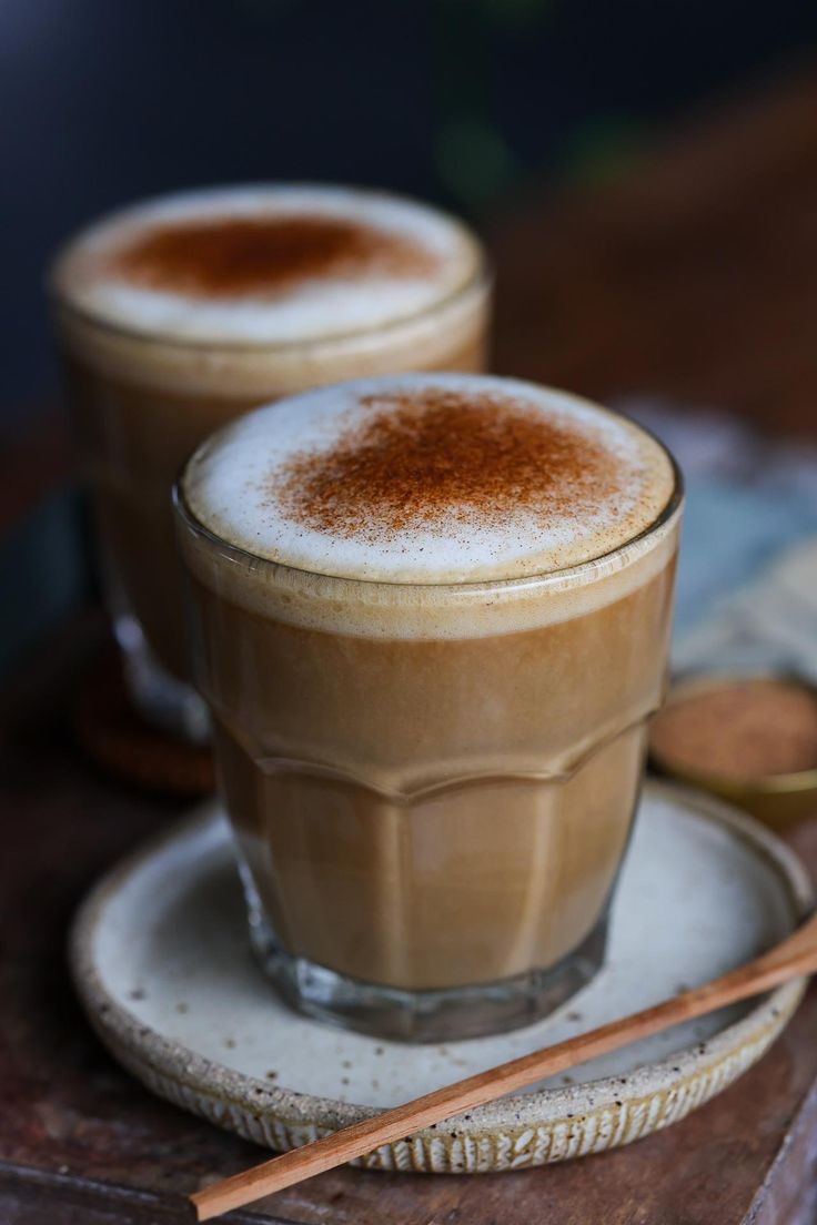 two glasses of hot chocolate on a plate with cinnamon sticks