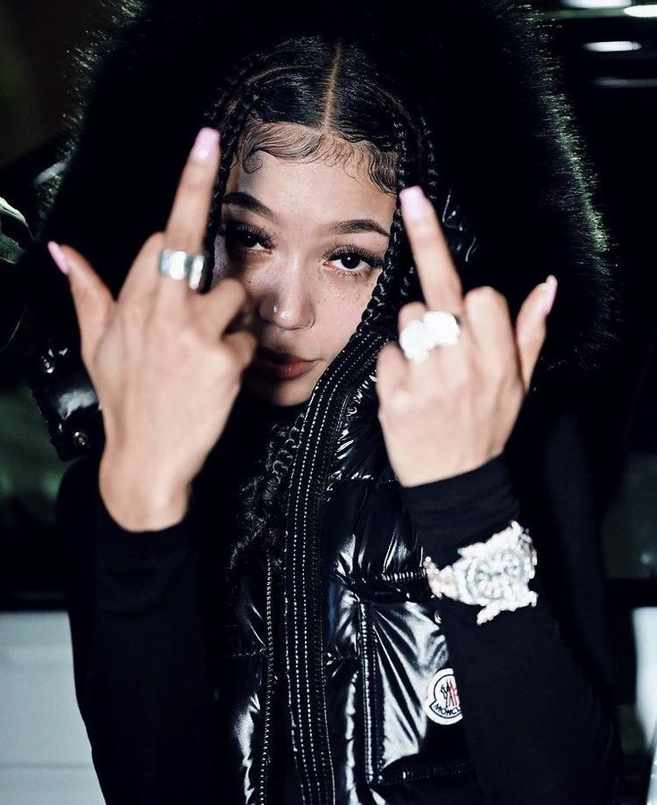 a woman with two fingers up in front of her face and wearing a black jacket