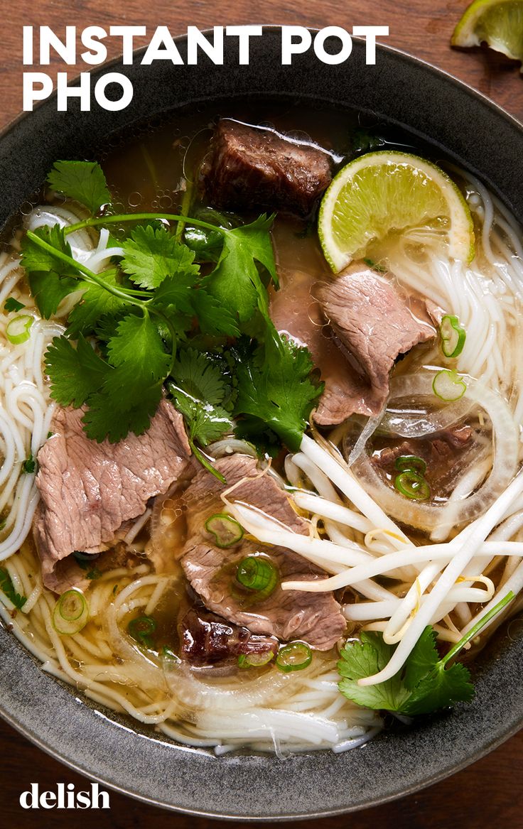 a bowl filled with meat, noodles and cilantros on top of a wooden table