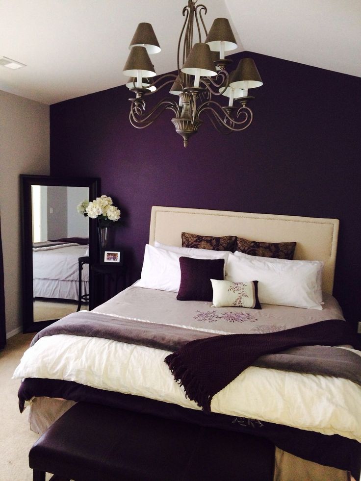 a large bed sitting under a chandelier next to a purple wall in a bedroom