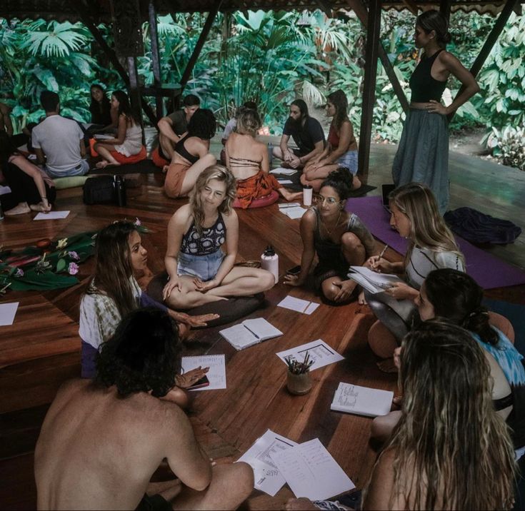 a group of people sitting on top of a wooden floor in front of some trees