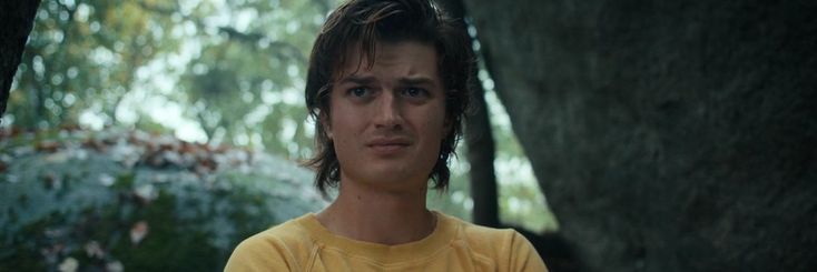 a young man in a yellow shirt standing next to a tree