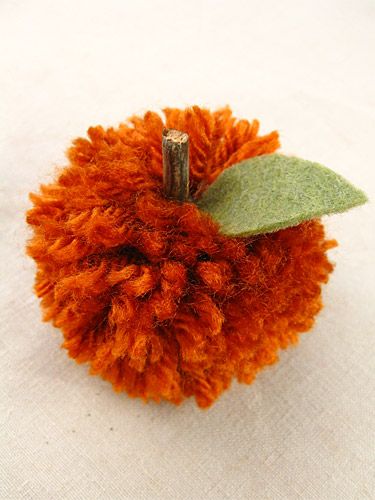 an orange pom - pom with a green leaf on it sitting on a white surface