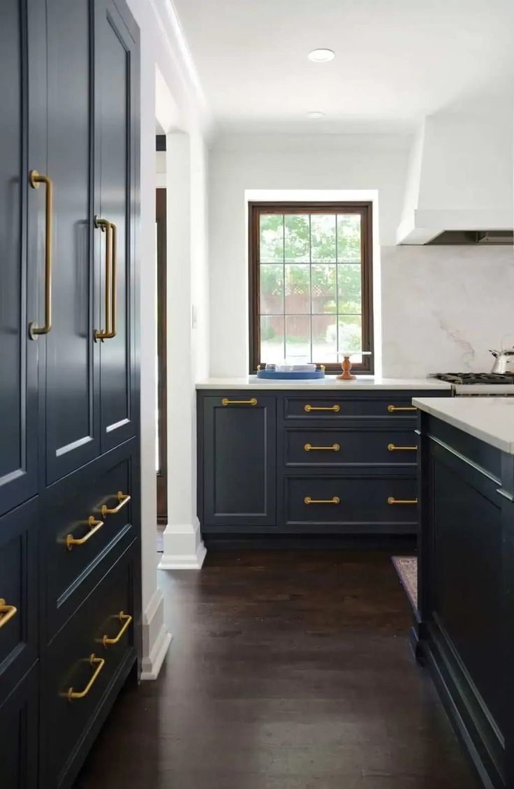 a kitchen with dark blue cabinets and gold pulls on the handles, along with marble counter tops