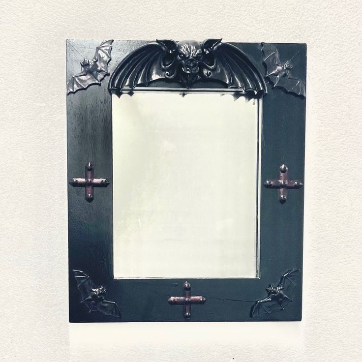 an ornate black frame with crosses and bats on the edges is shown in front of a white wall