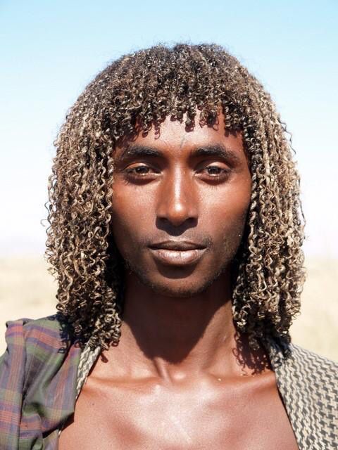 a man with long curly hair and no shirt is looking at the camera while wearing a jacket