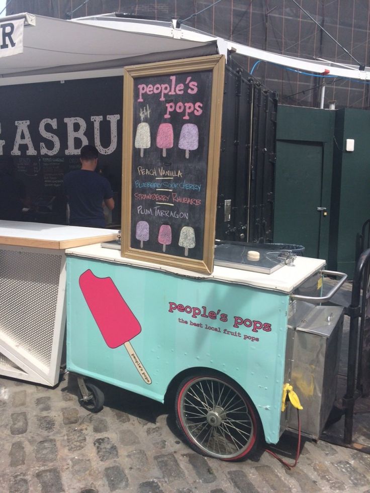 an ice cream cart is parked on the side of the street with people's pops written on it