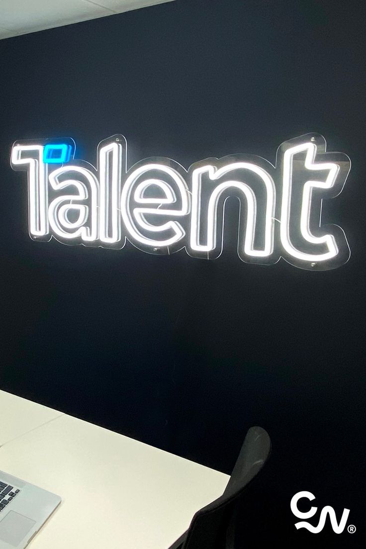 a laptop computer sitting on top of a desk next to a neon sign that says talent