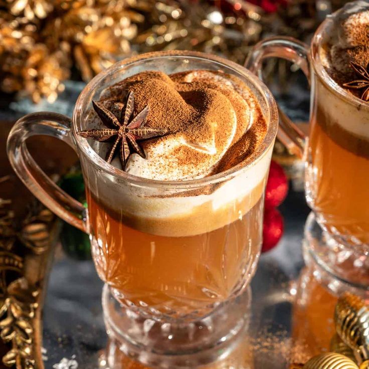 two mugs filled with hot chocolate and cinnamon sitting on a table next to christmas decorations