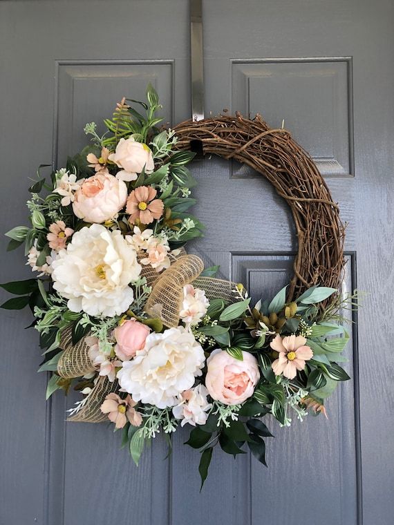 a wreath on the front door with flowers and greenery hanging from it's side