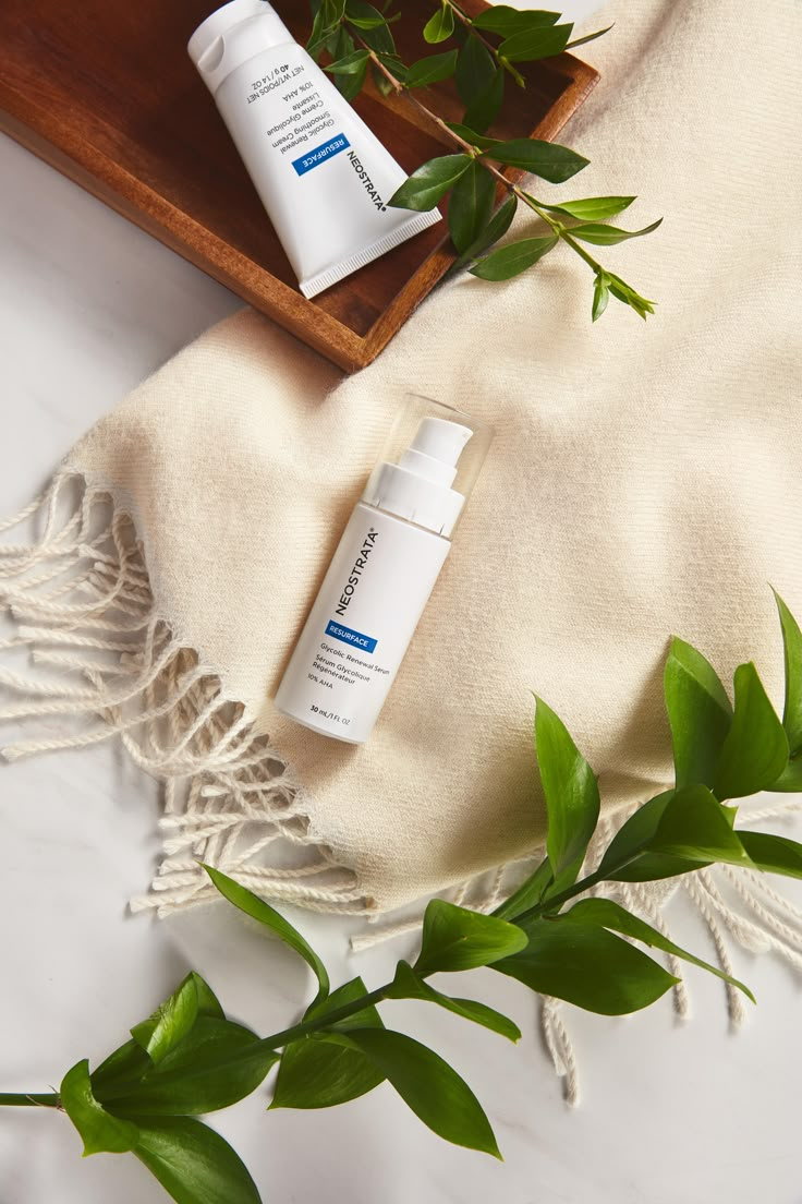 two bottles of skin care sitting on top of a wooden tray next to green leaves