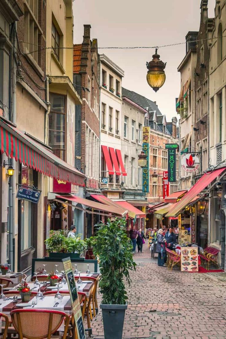 an empty street with tables and chairs in the middle, people are walking around it