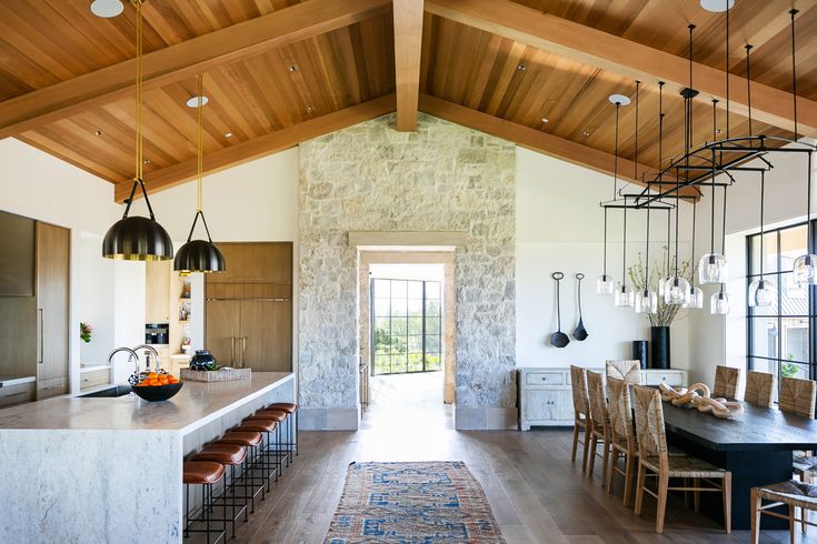 an open kitchen and dining room area with wood ceilinging, stone walls, and exposed beams