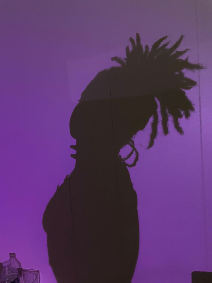 the shadow of a person with dreadlocks on their head in front of a purple background