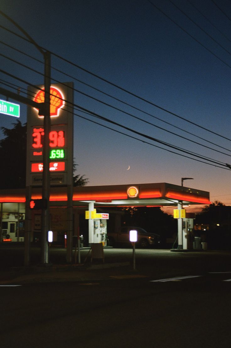 an empty gas station at night with the lights on and power lines in the background