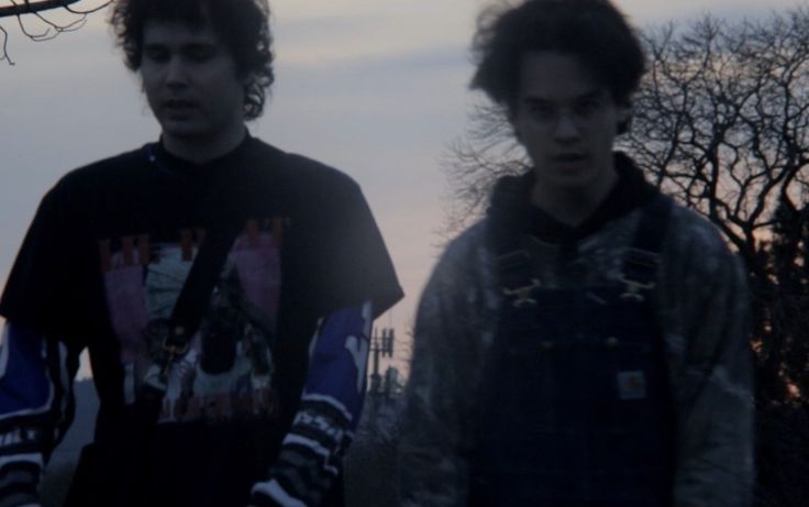 two young men standing next to each other in front of trees and fenced area