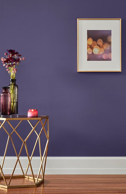 a table with vases and flowers on it in front of a purple painted wall