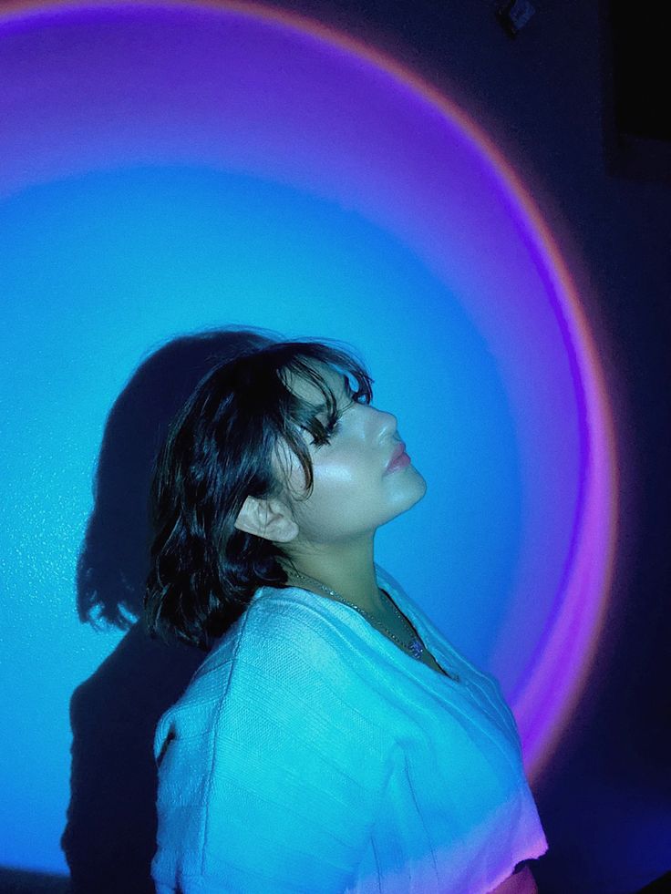 a woman standing in front of a blue and purple circular light with her eyes closed