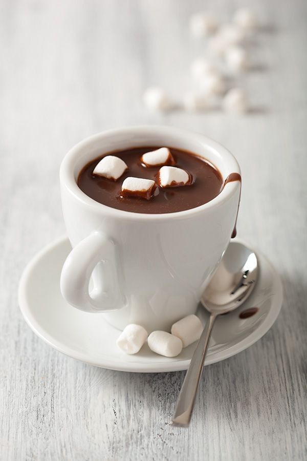 a cup of hot chocolate with marshmallows on the saucer and spoon