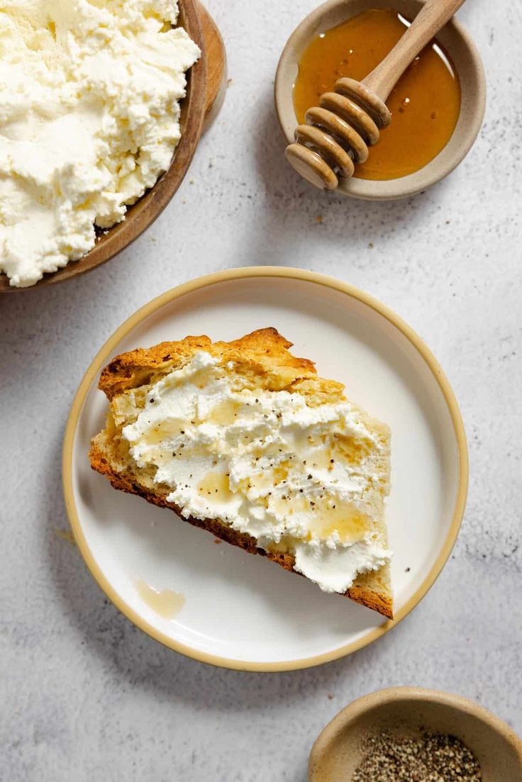 a piece of cake on a plate with whipped cream and honey in the bowl next to it