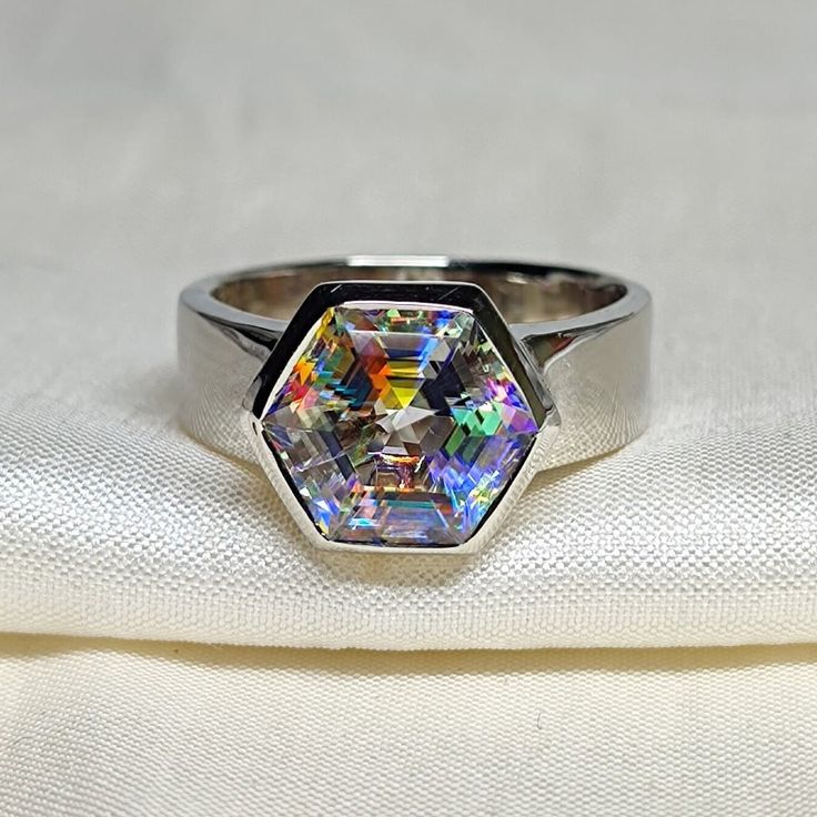 a ring with an iridescent colored diamond in the center on a white cloth