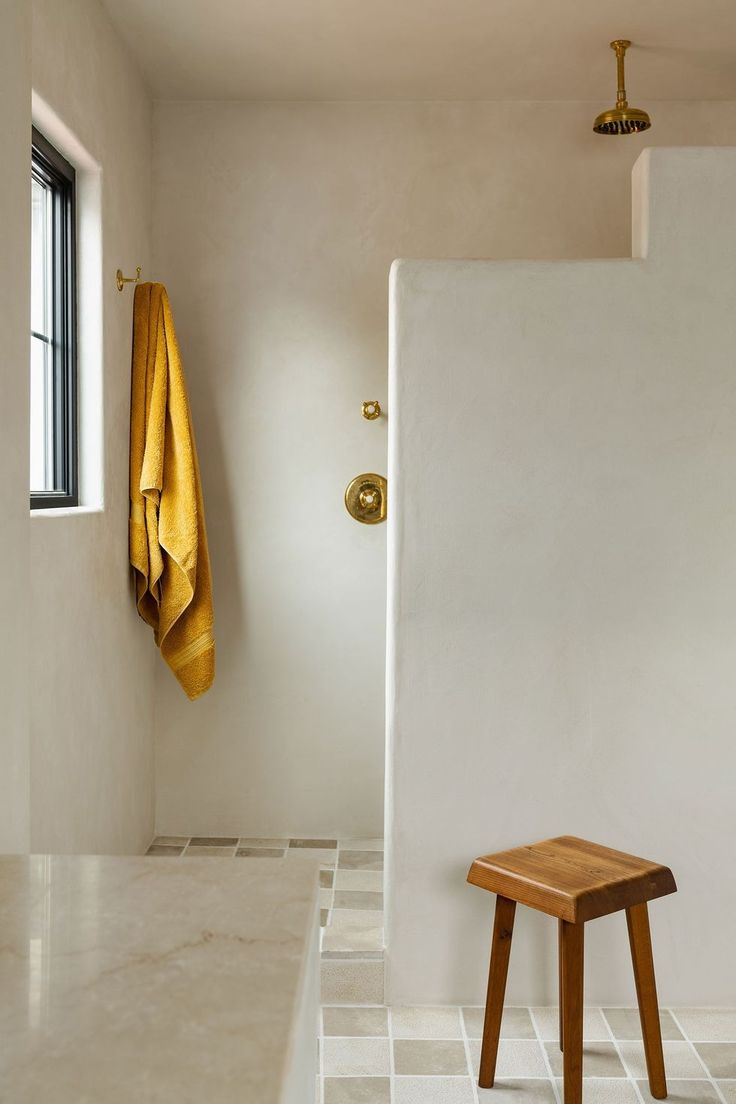 a wooden stool sitting in front of a window next to a white tiled bathroom floor