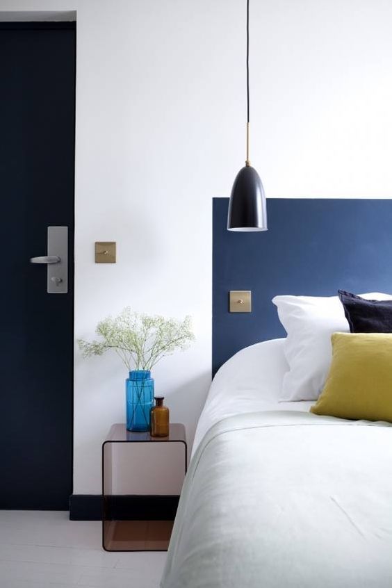 a bed with white sheets and blue headboard next to a lamp on the wall