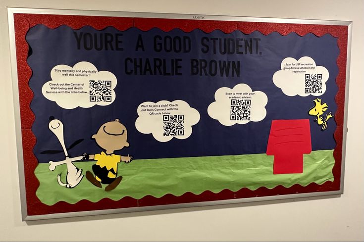 a bulletin board with a charlie brown theme and qr code on the front, reading you're a good student