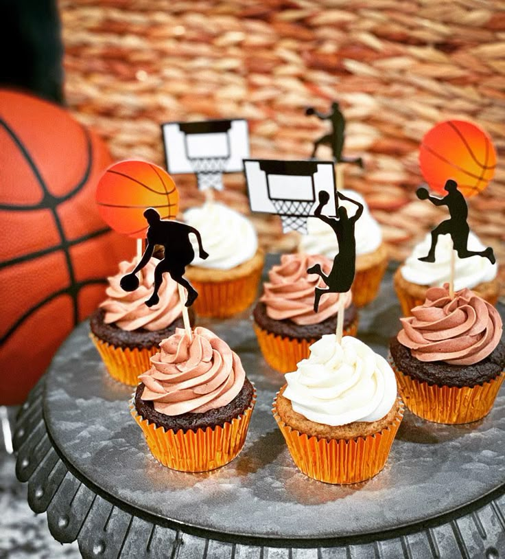 cupcakes with pink frosting and black silhouettes on top are sitting in front of a basket ball